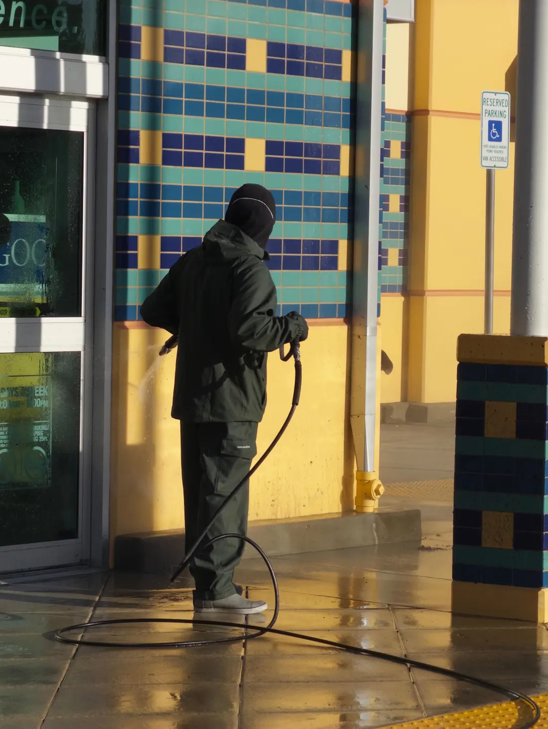 Crew member pressure washing a storefront entry and sidewalk